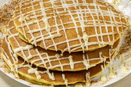 Sin-O-Man Pancakes — a stack of cinnamon pancakes with cream cheese icing and a cinnamon sprinkle